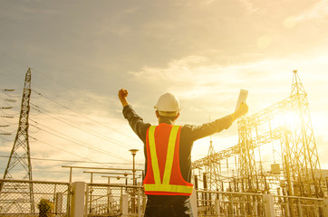 Electrician proudly raise their hands at the power substation against the sunrise background.