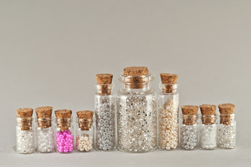White, beige and yellow beads in glass jars on a gray background. Beads in a transparent container with a wooden cork.