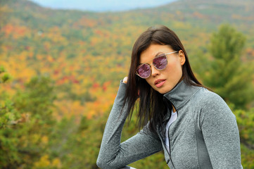 Outdoor portrait of glamour young brunette woman in sporty outfit and sunglasses posing at autumn park with beautiful foliage on the background.