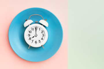 Fototapeta na wymiar Intermittent fasting concept. White alarm clock on empty blue plate. Top view, copy space