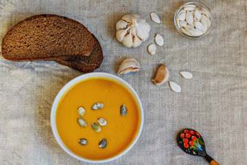 Composition on a homemade linen linen made of pumpkin puree soup, garlic, black bread, pumpkin seeds. Still life.