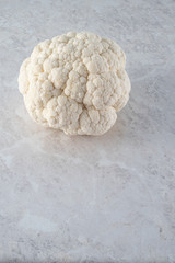 A large, fresh head of cauliflower on a light marble background. The concept of the diet.