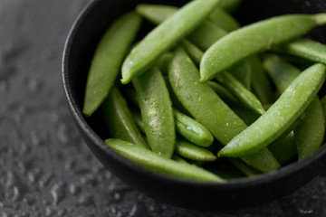 vegetable, food and culinary concept - close up of peas in bowl on wet slate stone background
