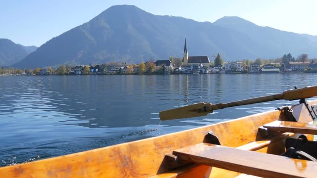 A peaceful picture a wooden boat with an oar floats on beautiful mountain lake Tegernsee against backdrop of the Alpine mountains and the picturesque container of the church. Ferryman ferries people