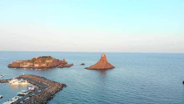 Aerial tracking forward, marina and tall rocky island off coast of Sicily