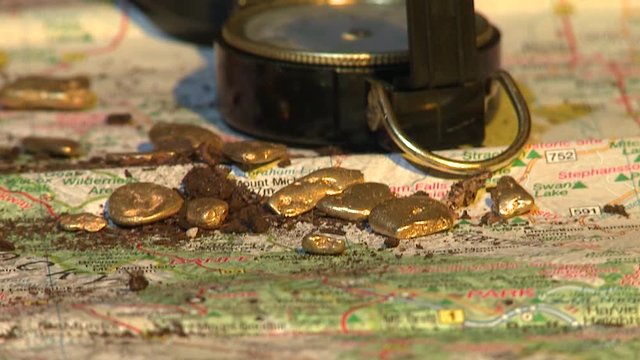 Close-up panoramic view from bottom to top of Gold nuggets on a map with a compass. Alberta, Canada. 60fps front view.