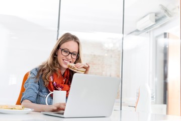Businesswoman eating sandwich and drinking coffee while working in office