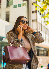 Attractive woman with long hair and sunglasses speaks on the phone in the street.