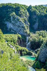 Fototapeta na wymiar Waterfall and blue crystalline water in Plitvice Nation Park (Croatia) in a sunny day in summer during vacations immersed in wild nature with rocks trees flowers and forests