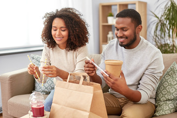 eating and people concept - happy african american couple with takeaway food and drinks at home