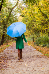 Woman holding umbrella and fall leafs while walking in the park.	