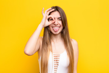 young pretty woman smiling happily with funny face, joking and looking through peephole, spying on...