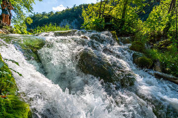 Waterfall and blue crystalline water in Plitvice Nation Park (Croatia) in a sunny day in summer during vacations immersed in wild nature with rocks trees flowers and forests