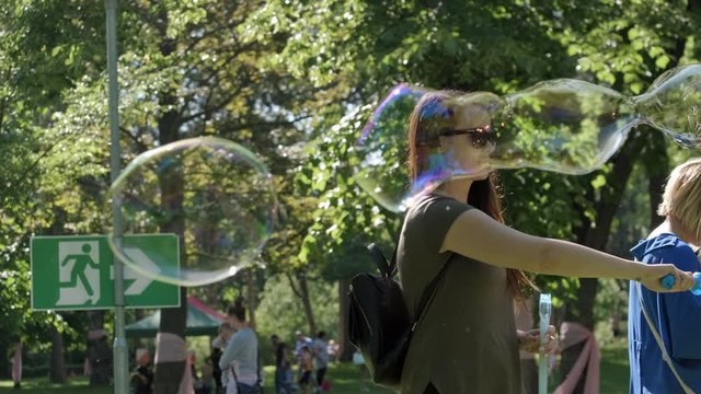Pretty woman making Colorful Big shimmering Soap Bubbles in the forest. Background Green Trees. Slow Motion. Prores 10Bit mov. Happiness moment.