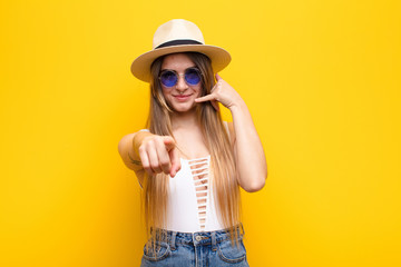 young pretty woman smiling cheerfully and pointing to camera while making a call you later gesture,...