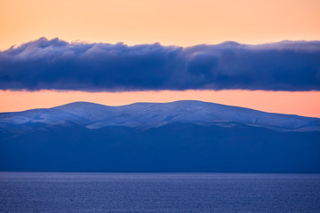 Fototapeta na wymiar Clouds over mountains and lake at sunrise