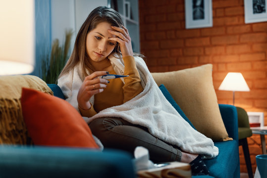 Young woman with cold and flu measuring her temperature