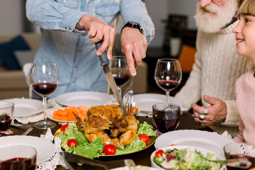 Cropped image of the hands of young father carving Thanksgiving turkey for his family sitting at the table