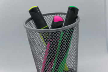 a metal glass in a grid in which there are three felt-tip pens of different colors (red, yellow and green). on white background. Background blurred