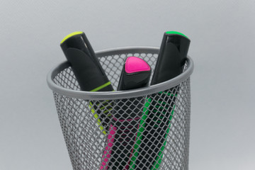 a metal cup in a grid in which there are three markers of different colors (red, yellow and green). on white background. Background blurred