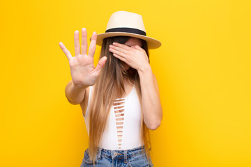 young pretty woman covering face with hand and putting other hand up front to stop camera, refusing...