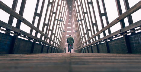 Man with bicycle on bridge - Commuter on bike over urban structure - Perspective of public wooden...