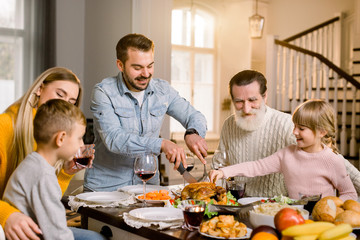 Obraz na płótnie Canvas happy excited family celebrating thanksgiving while cutting turkey