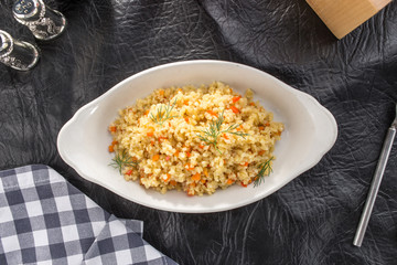 Cous cous with carrot in white bowl with tomato juice on black leather table
