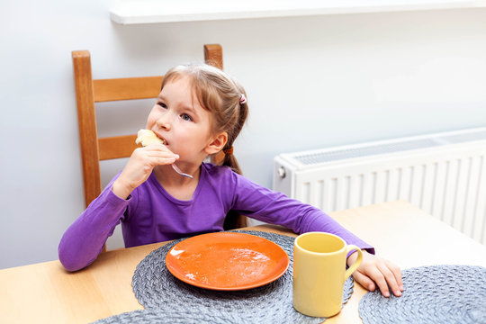 One Child, Small Girl Finishing Her Meal, Taking One Last Bite Using Fork Eating By Herself. Sitting On A Chair In Front Of An Empty Plate And A Tea Cup. Making Faces, Happy Solo Meal Appetite Concept