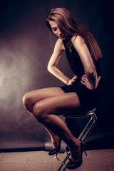 portrait of a young girl sitting on a bar stool with long hair in dark colors