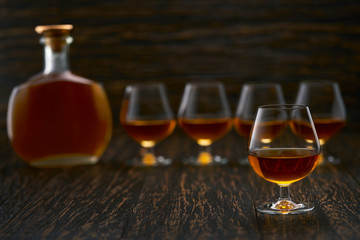 Full glass of cognac in the background, three glasses of cognac and a full bottle of cognac.