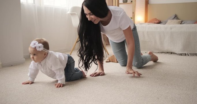 Happy mother with baby daughter crawling on carpet in the bedroom