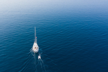 Motor-sailing mini yacht with a rescue boat tied to it floats on the sea. The view from the top.