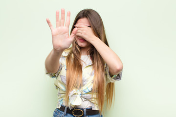 young pretty woman covering face with hand and putting other hand up front to stop camera, refusing...
