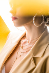 cropped view of young woman in necklace and earrings on orange and white