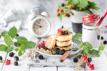 Homemade pancakes with berries, the blackberries, the honey on the plate, a branch of a BlackBerry alarm clock on white wooden background