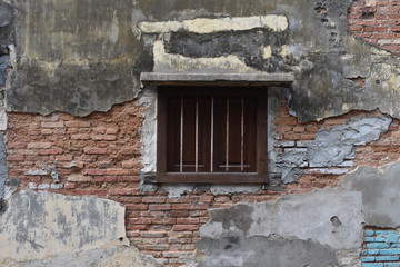 Old wooden windows with anti-theft steel on the broken old concrete wall reveals a red brick inside.