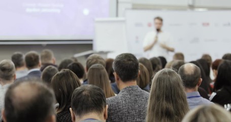 Blur background of educational business training. Student science conference at university campus, man speaker talks microphone for audience, explaining and writing on white board, view from viewers.