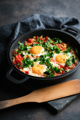 Traditional  shakshuka with eggs, tomato, and parsley in a iron pan on a dark background