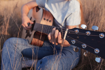 Girl plays the acoustic guitar in the field on sunset. Fingers on guitar fretboard. Nature and...