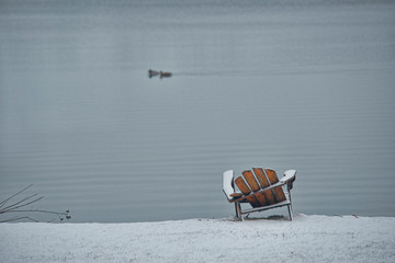 Fototapeta na wymiar Empty Adirondack Chair with Snow at Edge of Lake, Series