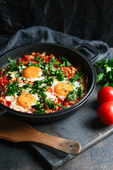 Traditional  shakshuka with eggs, tomato, and parsley in a iron pan on a dark background