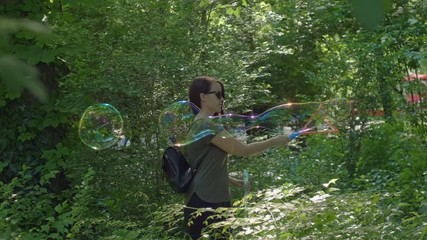 Pretty woman making Colorful Big shimmering Soap Bubbles in the forest. Background Green Trees. Slow Motion. Prores 10Bit mov. Happiness moment.