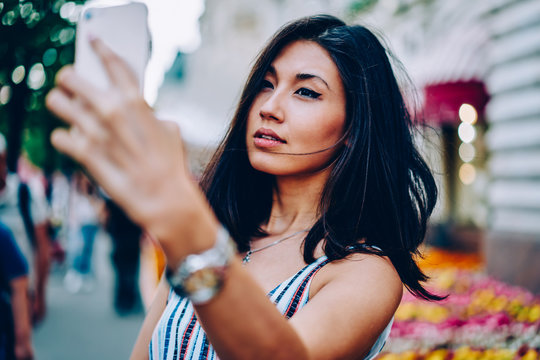Attractive asian woman posing for selfie on modern smartphone camera while strolling on street,beautiful young girl using application on mobile for making cool images and share in social  networks