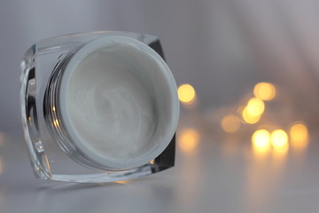 Closeup of facial moisturiser in a glass jar with fairy lights in the foreground. Concept of winter skincare. 