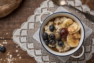 Porridge close-up on wooden table. Ingredients: oat flakes, banana, blueberries, chia, cinnamon, maple syrup and strawberry jam. Horizontal. Top view