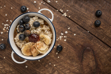 Vegan porridge on wooden table with oat flakes, banana, blueberries, chia, cinnamon, maple syrup and strawberry jam. Horizontal. Top view. Copyspace