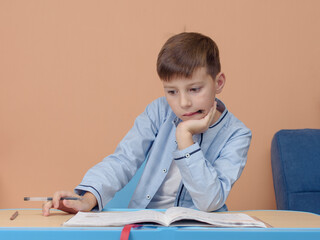 European boy sitting at the desk he is doing his home assignment. He is trying to solve difficult task.