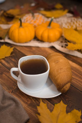 Cup of tea with croissant and pumpkins on the table.