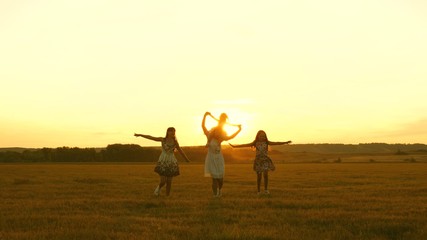 happy childhood concept. Happy young family with a child run across field in flight at sunset light. Mother and daughters walks in park and play in the meadow in sun. concept of life of large family